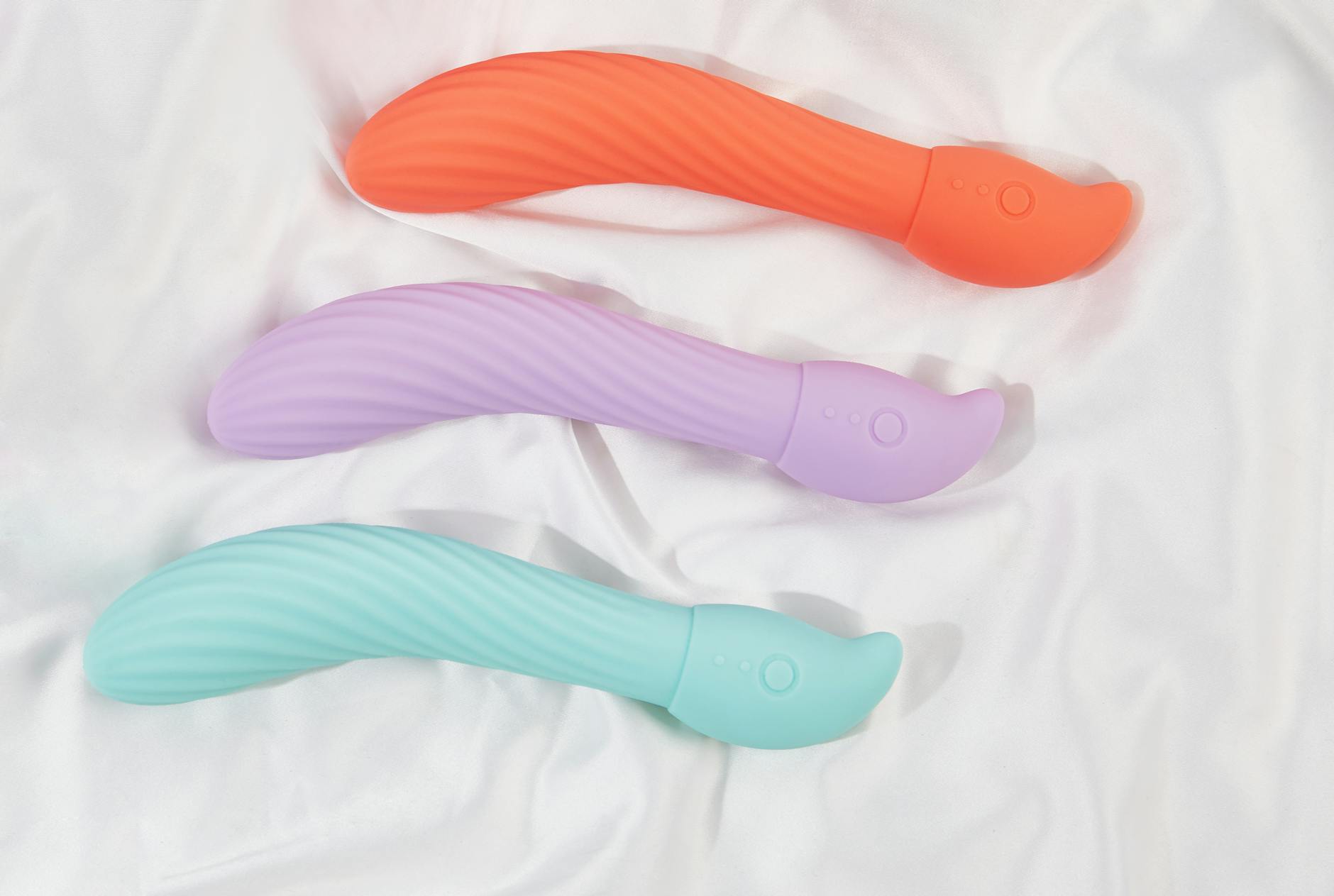 Three colorful clitoral vibrators arranged on soft white fabric, showing different toy designs.