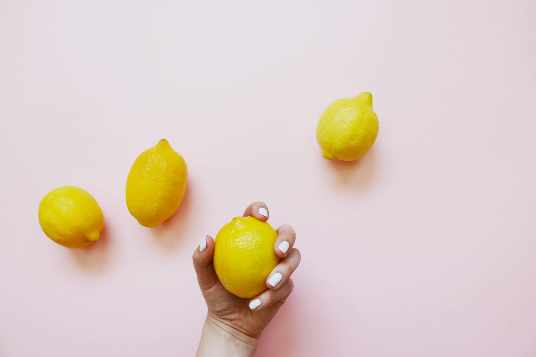 Hand holding a fresh lemon on soft pink background, symbolizing new beginnings and self-discovery