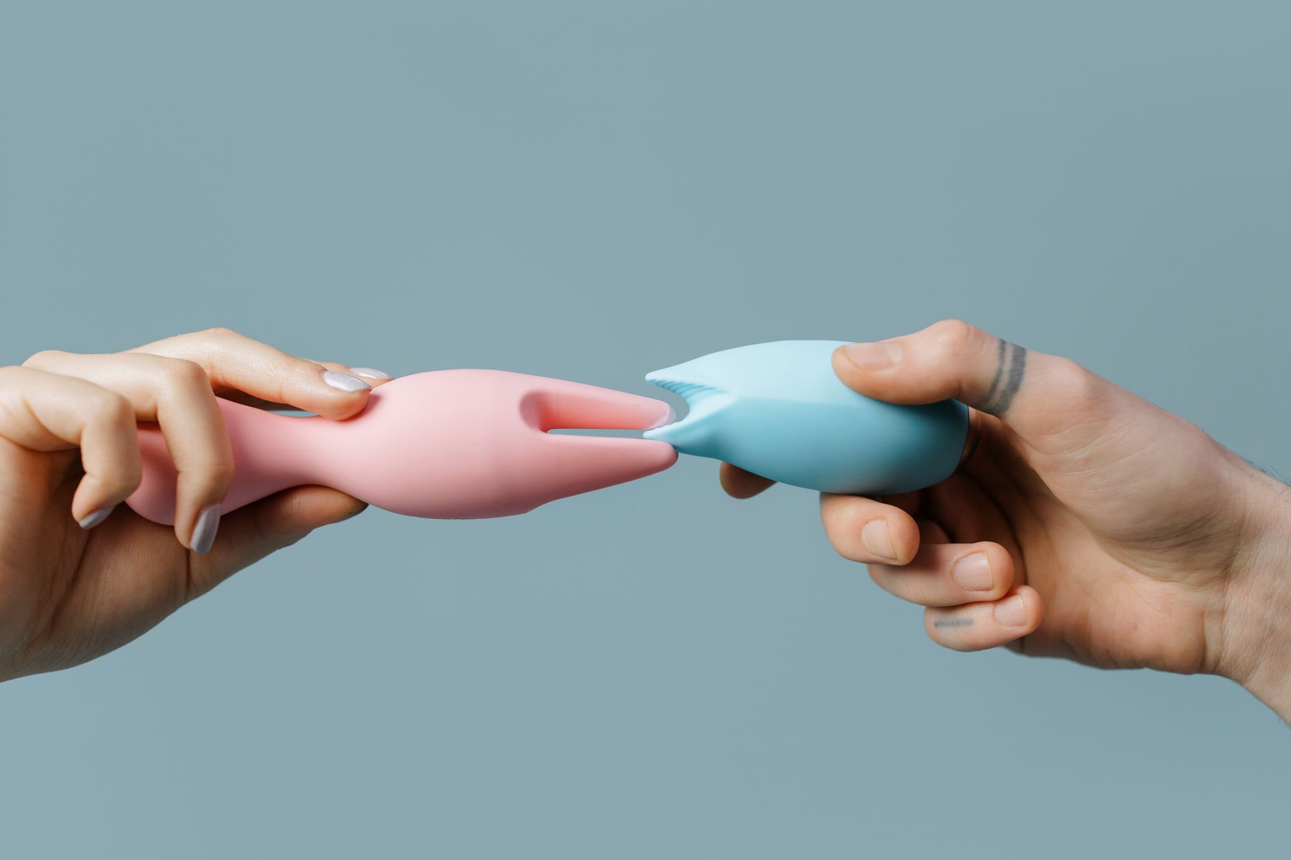 Manos sosteniendo juguetes sexuales de silicona en colores pastel