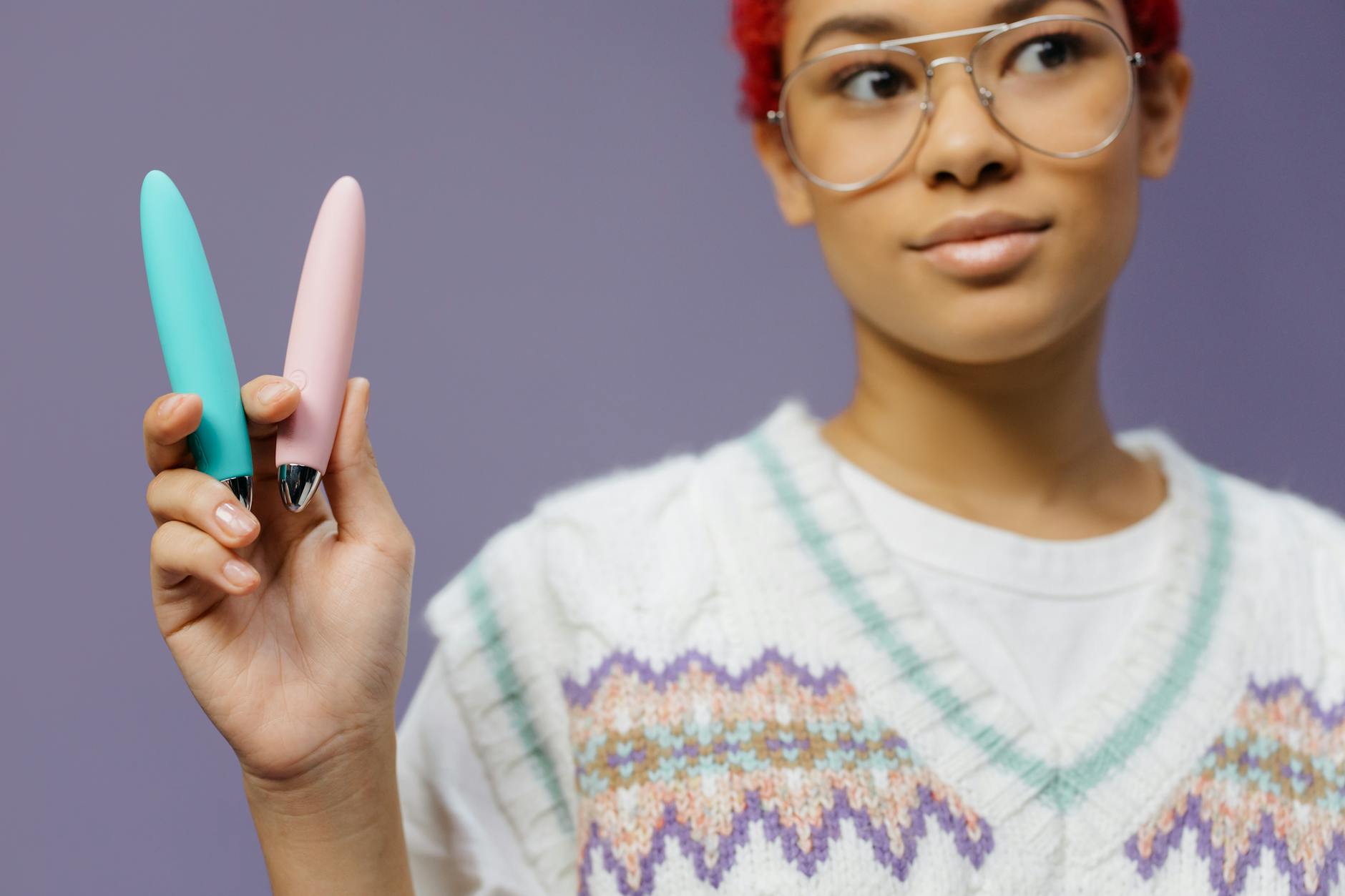 Two colorful clitoral vibrators held together against a purple background