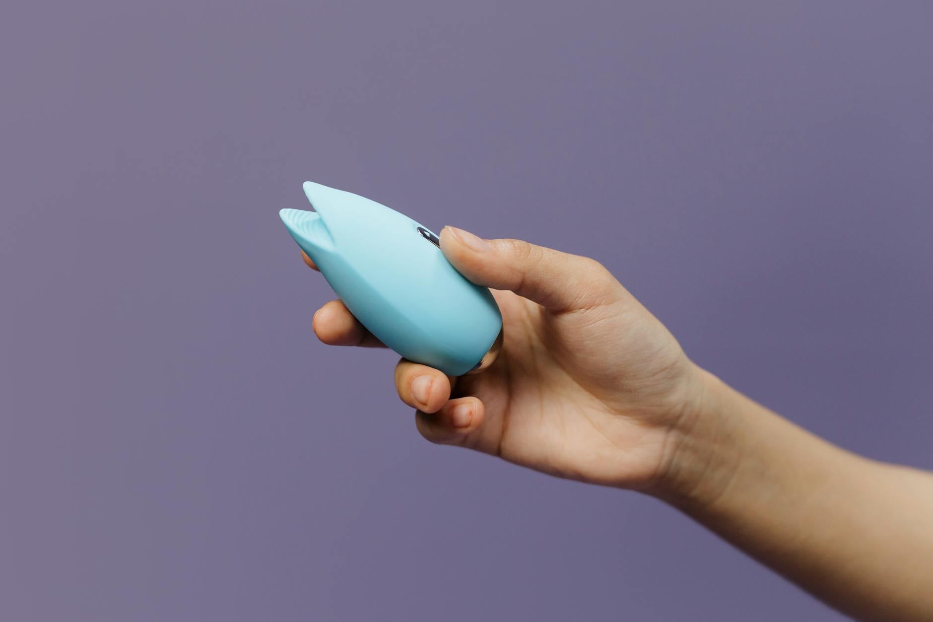 A hand holding a sleek vibrator against a purple background, representing pressure-free intimate exploration