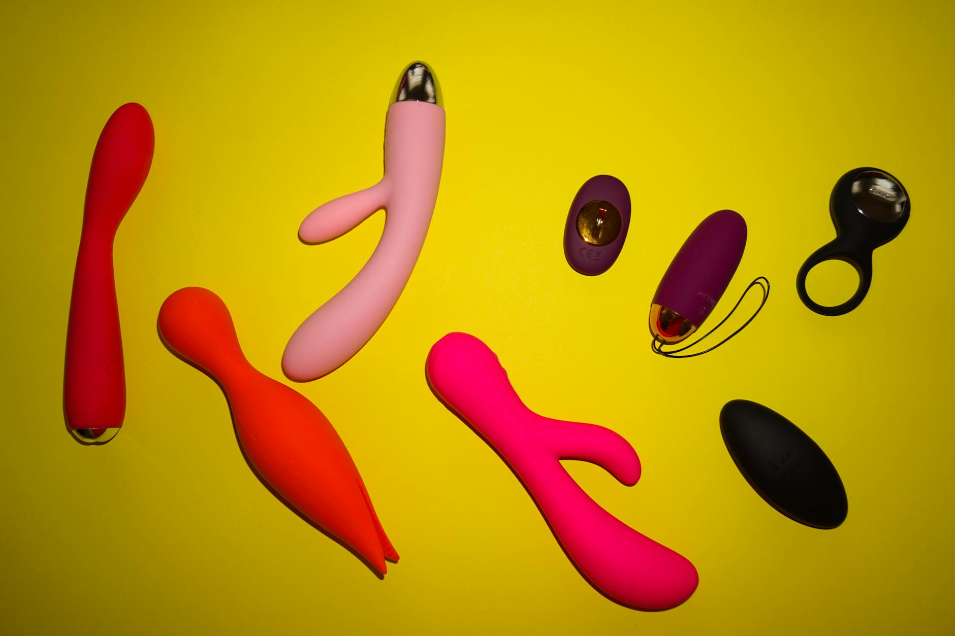 Array of colorful clitoral vibrators and toys arranged on bright yellow background