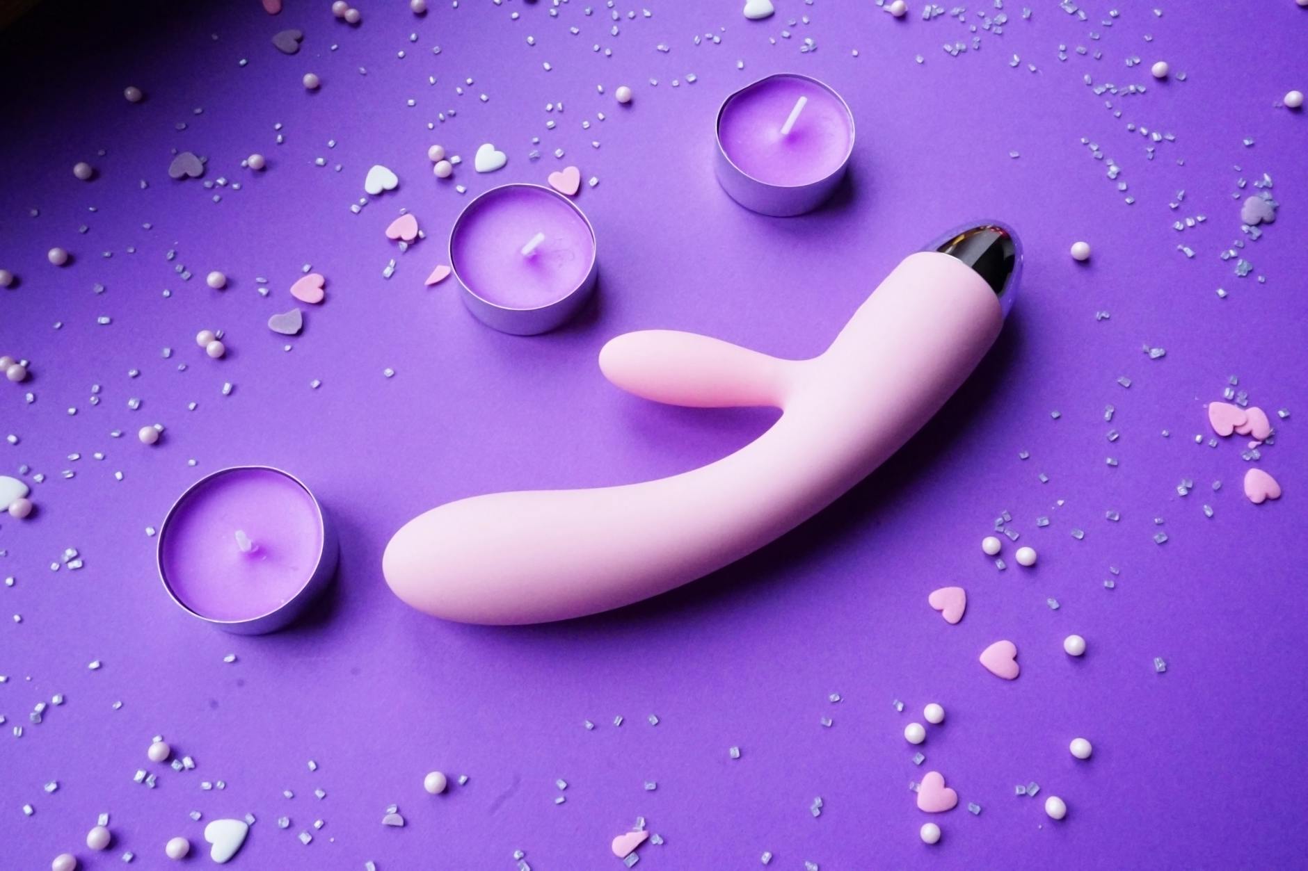 Pink lemon vibrator on purple background with heart confetti and candles for romantic reconnection